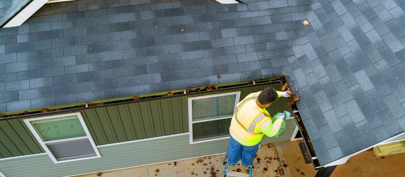 A worker is cleaning clogs in roof gutter drain by picking up dirt, debris, fallen leaves