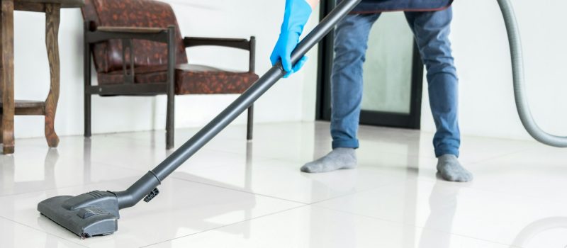 Young attractive man is cleaning vacuum commercial cleaning equipment on floor at home helping wife